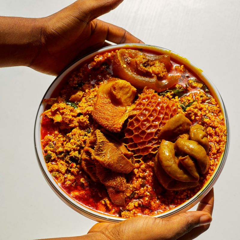 Hands holding a bowl of Nigerian soup served with assorted meats