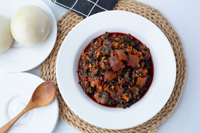A bowl of Nigerian vegetable dish with meat, served with a wooden spoon